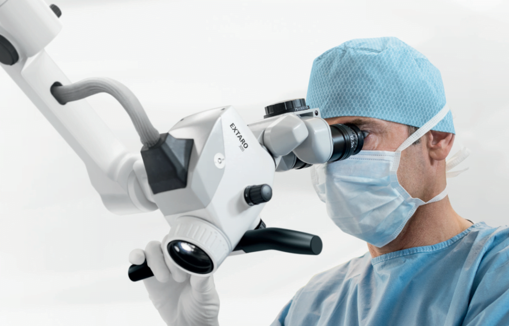 man in dentistry scrubs and protective gear looking through microscope